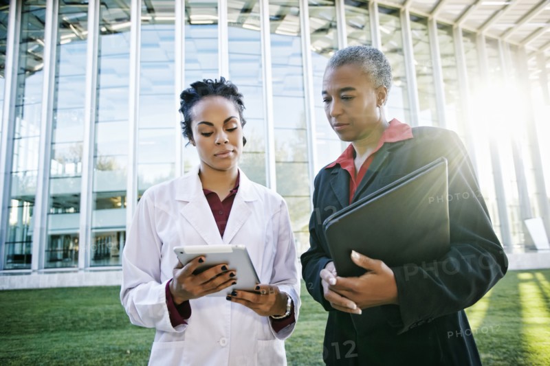 Doctor and administrator outdoors at hospital using digital tablet