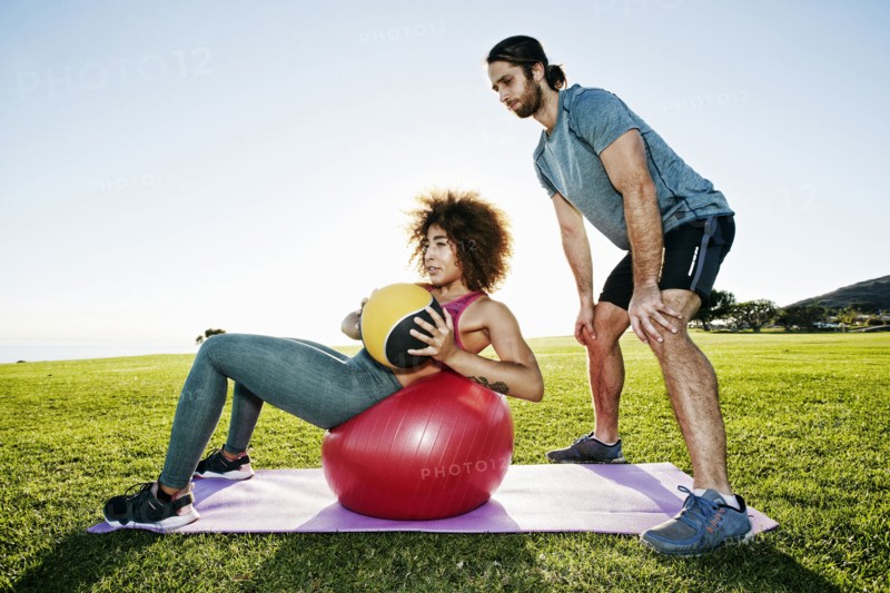 Couple exercising with fitness ball and heavy ball in sunny field