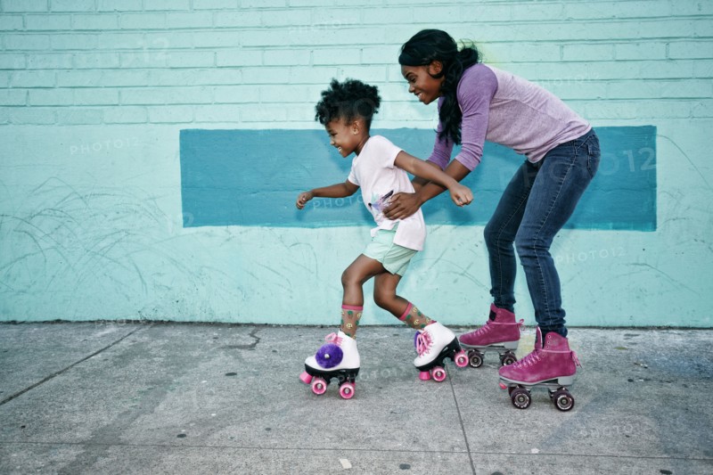 Black mother holding waist of daughter wearing roller skates