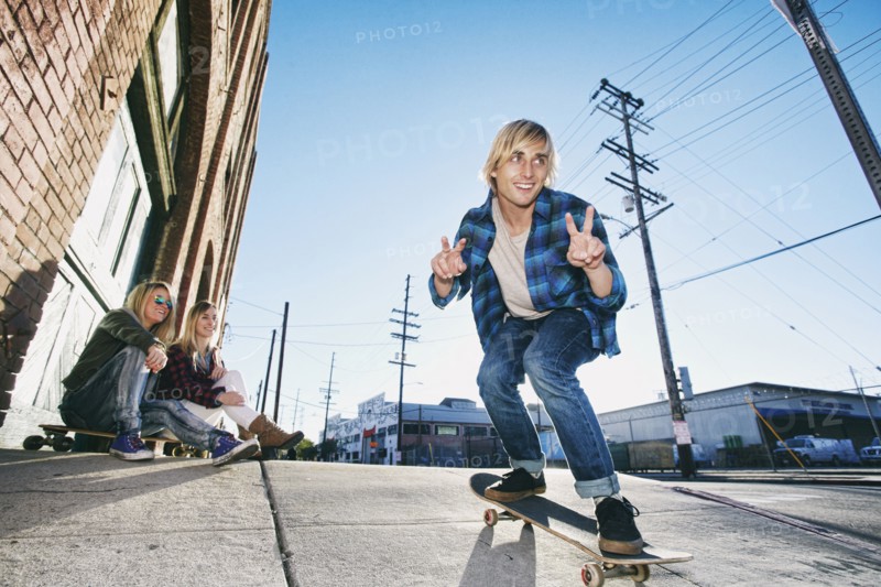Women watching man skateboarding on urban sidewalk