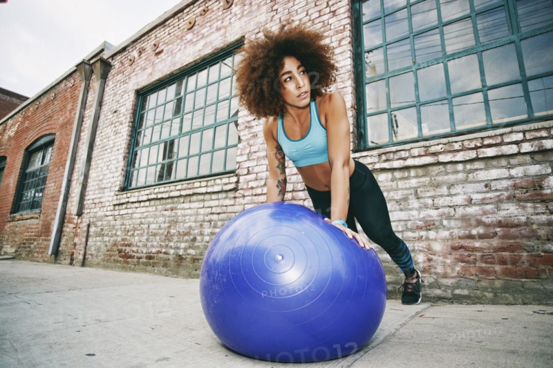 Hispanic woman balancing on fitness ball near brick wall