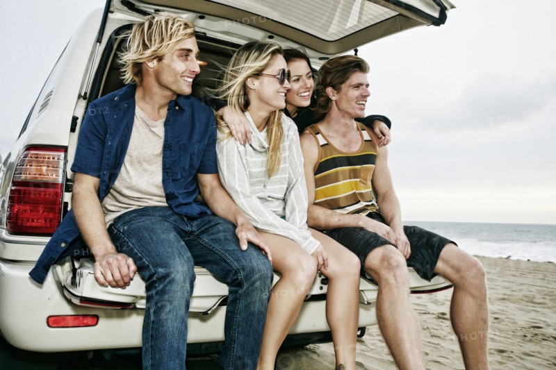 Caucasian friends sitting in car hatch at beach