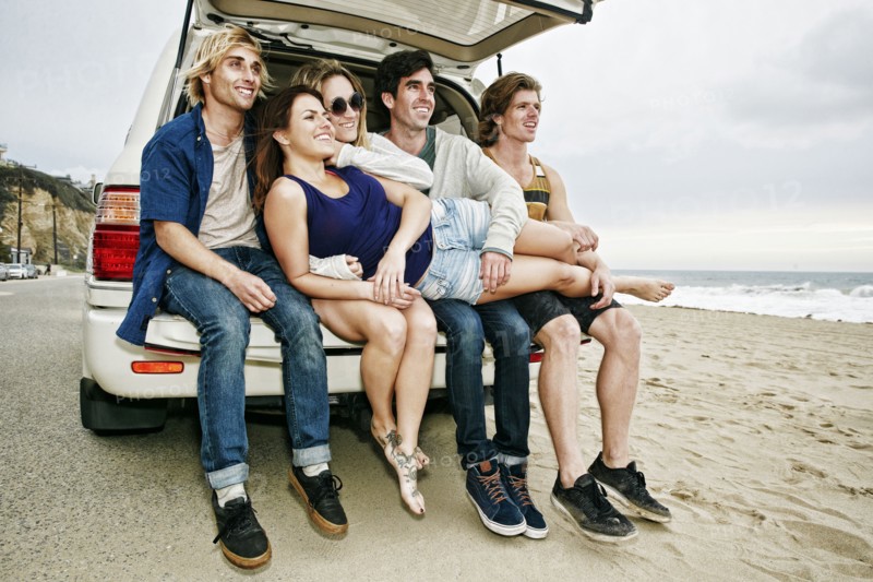 Caucasian friends sitting in car hatch at beach