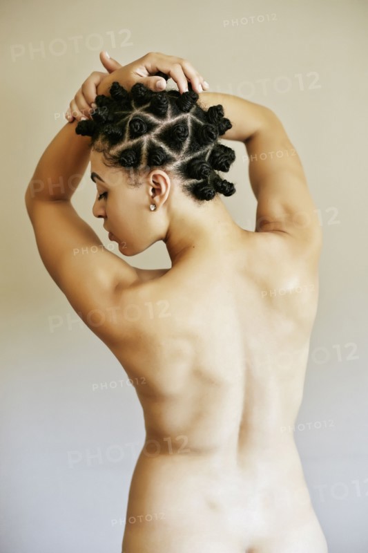 Rear view of naked Mixed Race woman with arms raised