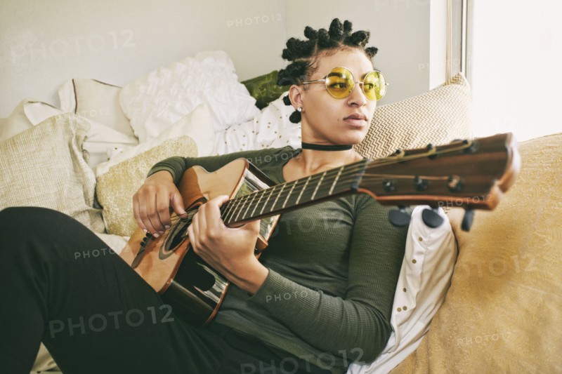 Mixed Race woman sitting on bed playing guitar