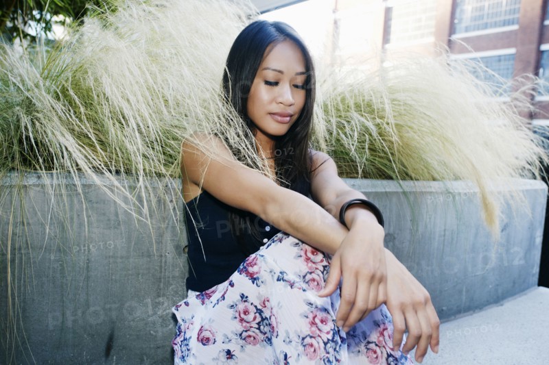 Pensive Asian woman sitting near foliage