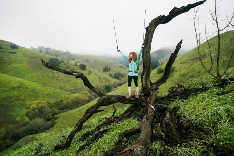 Caucasian woman standing on tree celebrating with walking sticks