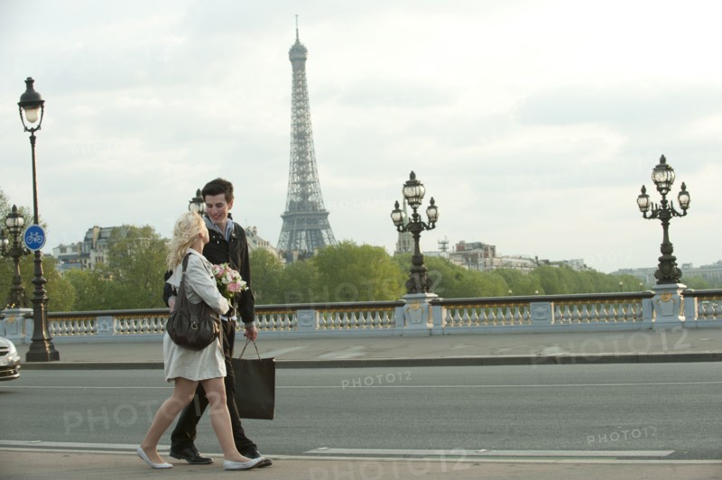 Caucasian couple walking across bridge with Eiffel Tower in background