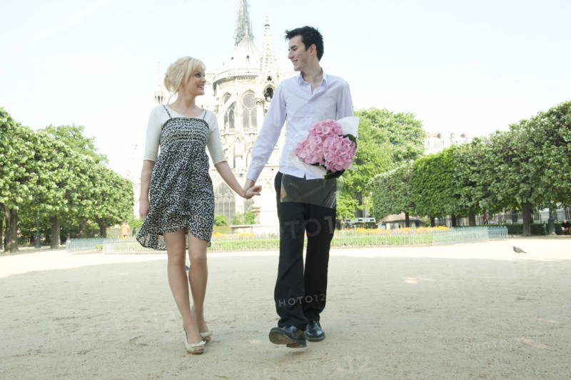 Caucasian couple holding hands in park near Notre Dame