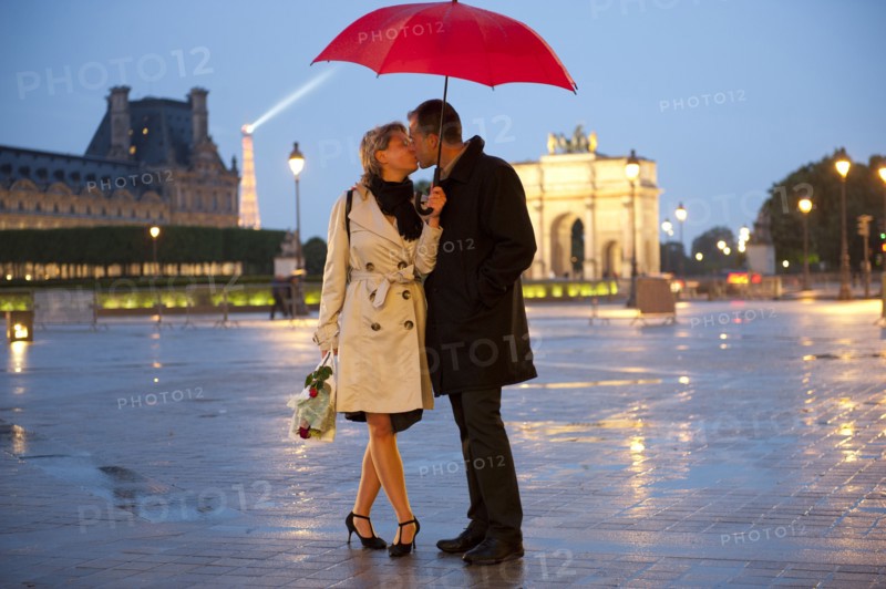 Caucasian couple kissing in rain at night near the Louvre