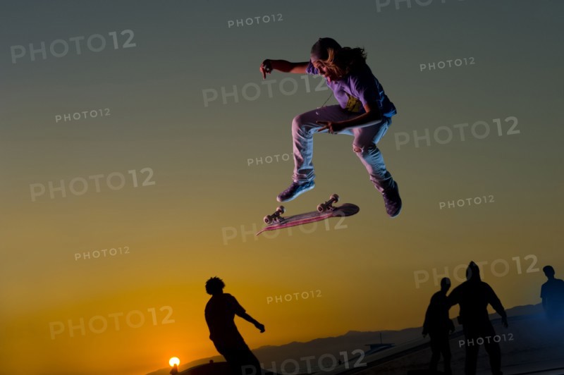 Skateboarder doing stunt in mid-air at sunset