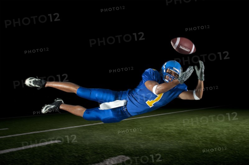 Mixed race football player jumping in mid-air catching football