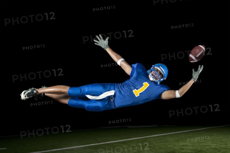 Mixed race football player jumping in mid-air catching football