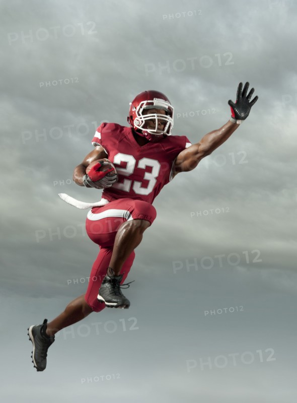 Black football player carrying football in mid-air