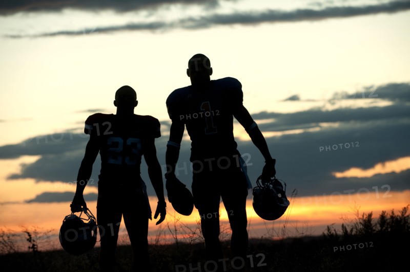 Silhouette of Black football players carrying helmet and football