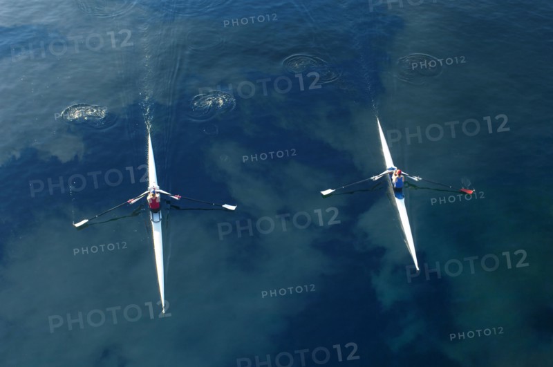 People rowing sculling boats on river