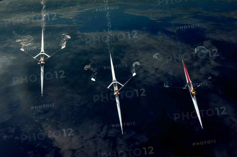 People rowing sculling boats on river