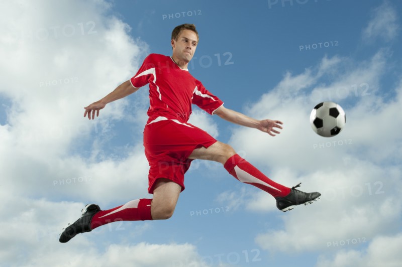 Soccer player jumping in mid-air kicking ball