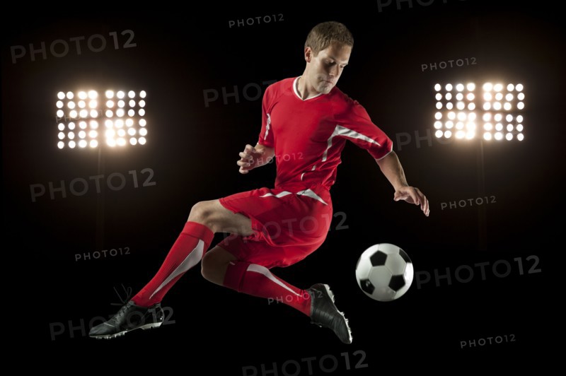 Soccer player jumping in mid-air kicking ball at night