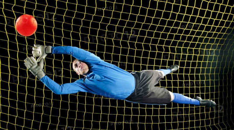 Caucasian soccer goalie jumping in mid-air catching ball at night