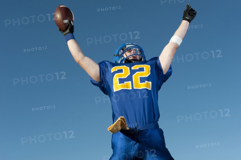 Caucasian football player holding football with arms raised