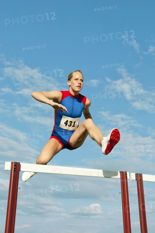 Caucasian runner jumping over hurdles on track
