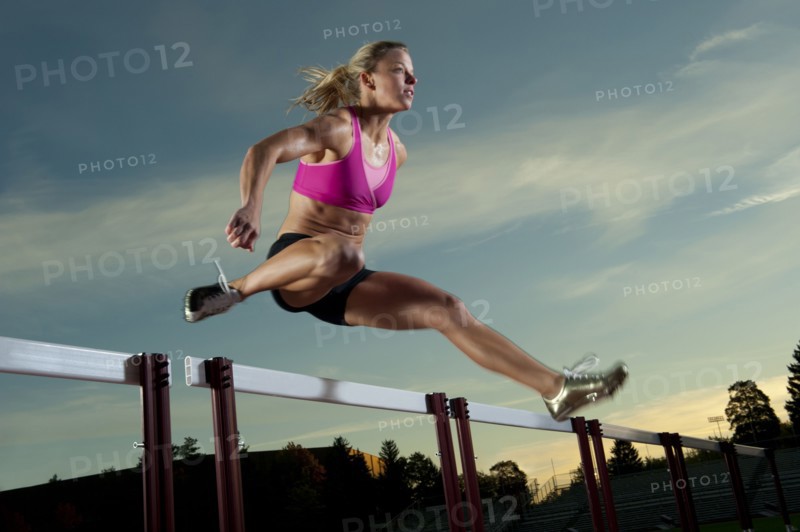 Caucasian runner jumping over hurdles