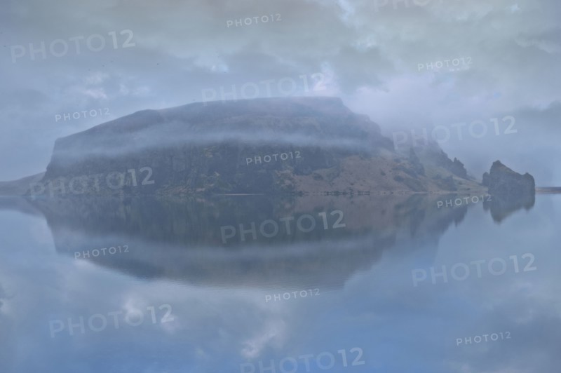 Snowy mountain under cloudy sky reflected in lake