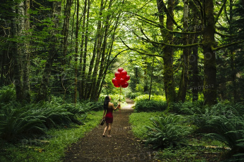 Korean woman holding red balloons in lush forest