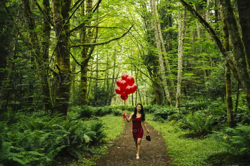 Korean woman holding red balloons in lush forest