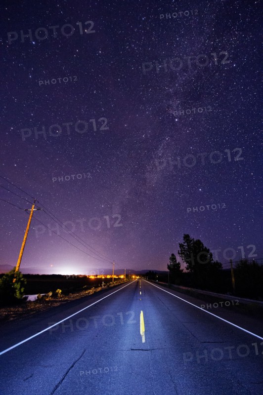 Paved road under starry night sky illuminated by headlights