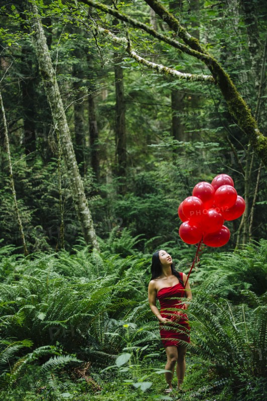 Korean woman holding red balloons in lush forest