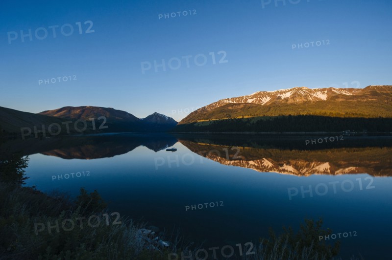 Remote mountains and blue sky reflected in still lake