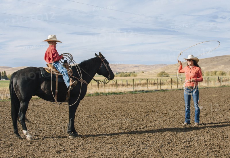 Caucasian woman teaching boy to use lasso on ranch