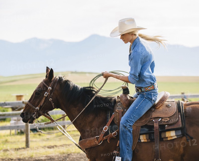 Caucasian cowgirl holding lasso on horseback