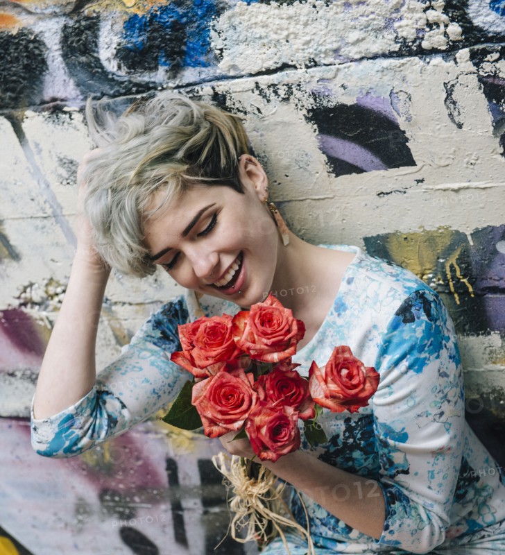 Laughing Caucasian woman at graffiti wall holding flowers