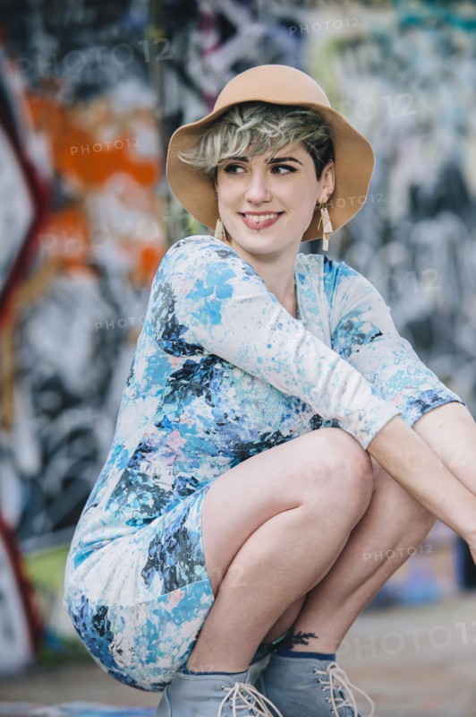 Smiling Caucasian woman crouching at graffiti wall