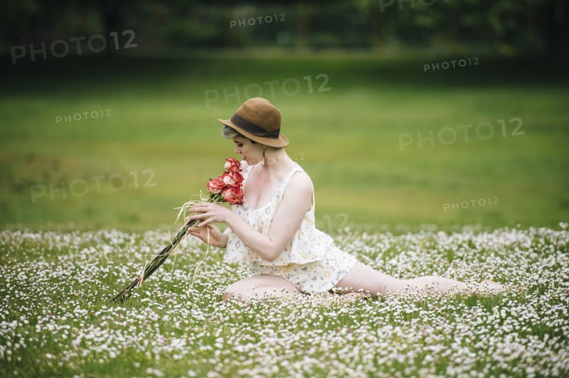Caucasian woman sitting in field of flowers smelling roses