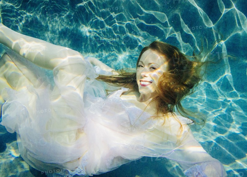 Caucasian woman wearing dress swimming underwater