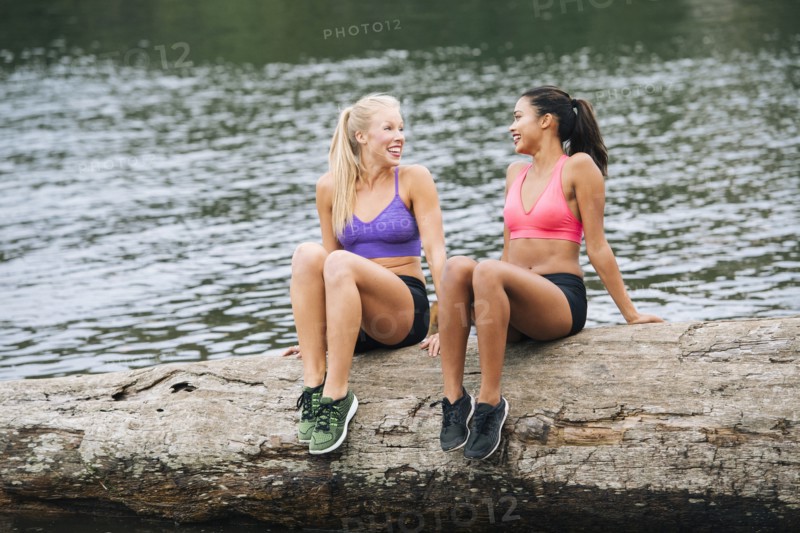 Smiling women sitting on log near lake