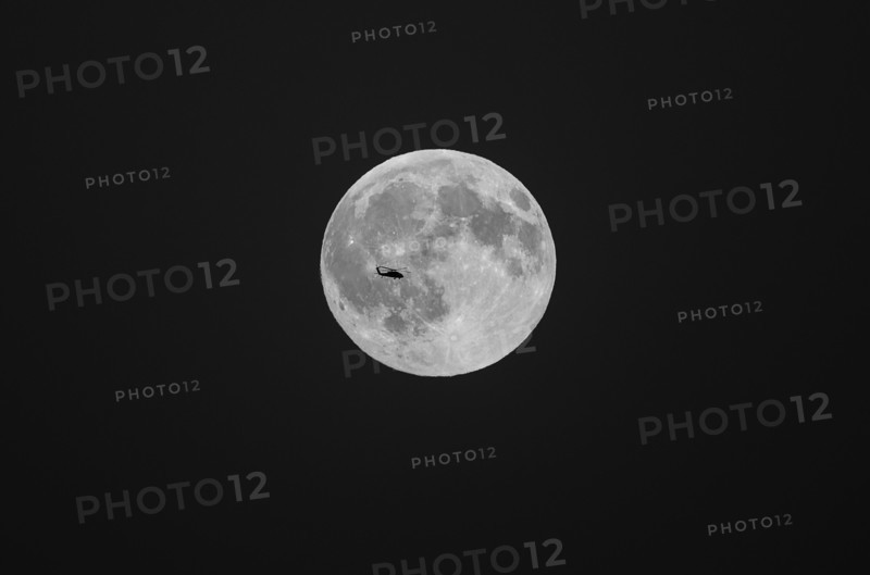 Silhouette of helicopter flying in front of full moon