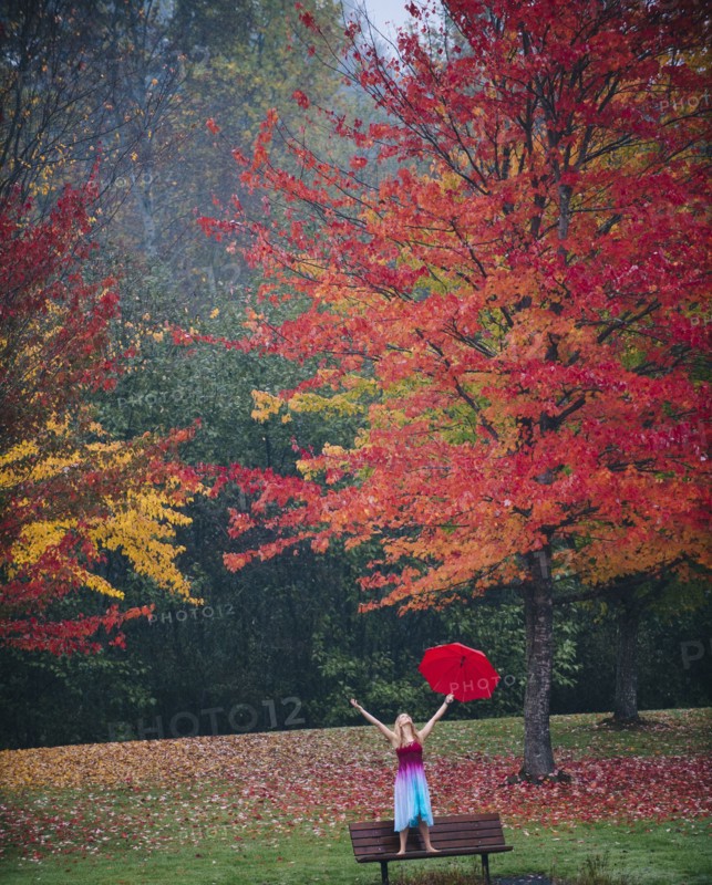 Caucasian woman holding umbrella in rain on park bench