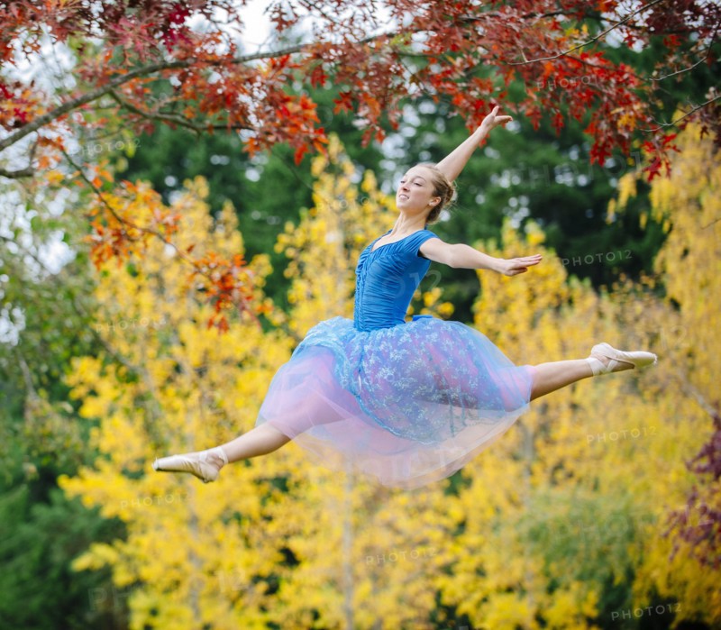 Caucasian ballerina leaping under branches in park