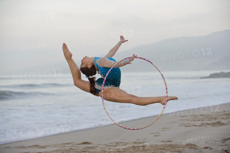 Caucasian gymnast jumping with hoop on beach