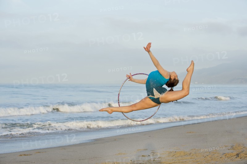 Caucasian gymnast jumping with hoop on beach