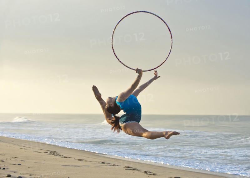 Caucasian gymnast jumping with hoop on beach