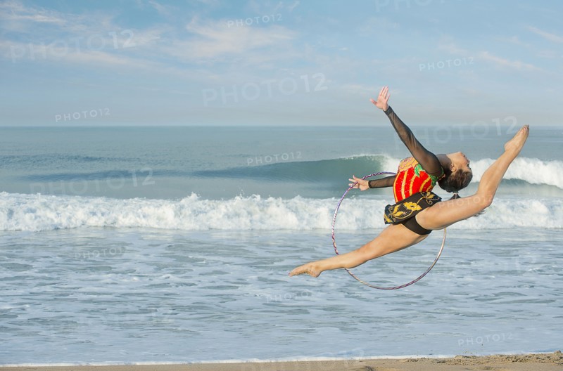 Caucasian gymnast jumping with hoop on beach