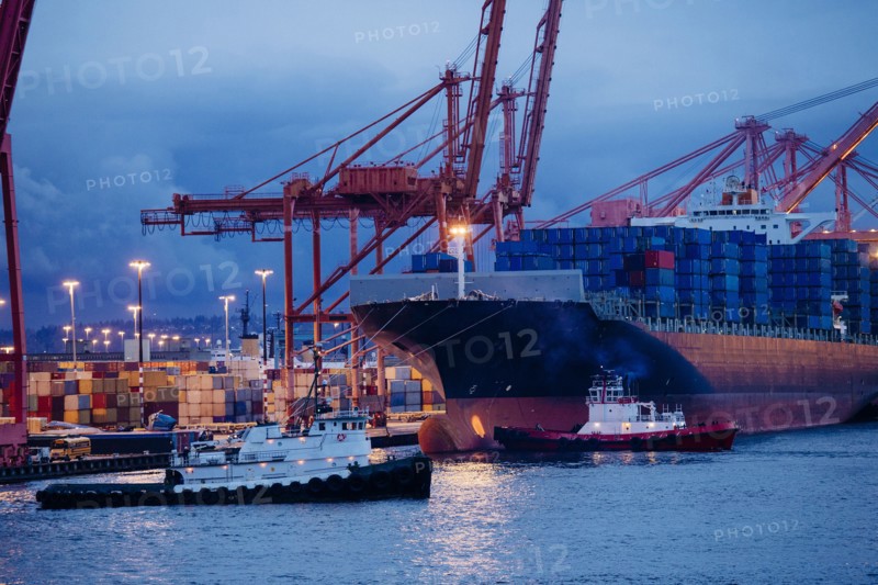 Cargo containers on freighter at shipping port near tugboats