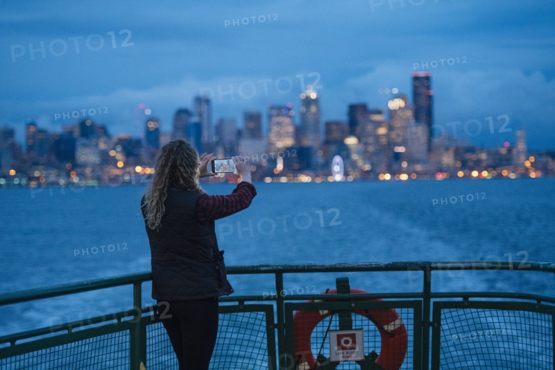 Caucasian woman on boat photographing urban waterfront with cell phone