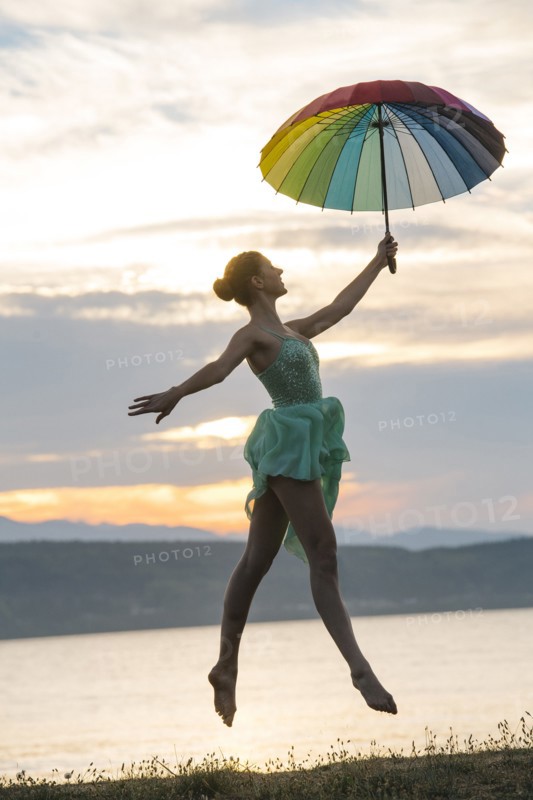 Caucasian ballerina jumping with multicolor umbrella on beach